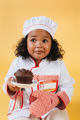 A little girl holding a chocolate muffin looking confused or pensive