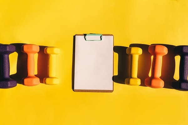 Clipboard and hand weights on yellow background