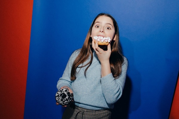 Woman guiltily eating junk food in front of blue wall