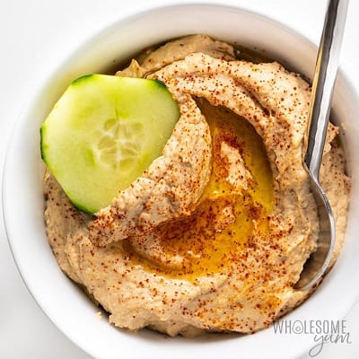 Roasted cauliflower hummus in a bowl with a slice of cucumber