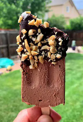 Keto chocolate ice cream bars in a person's hand with nuts on top
