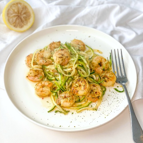 keto shrimp scampi with zoodles on a white plate with a half lemon in the background
