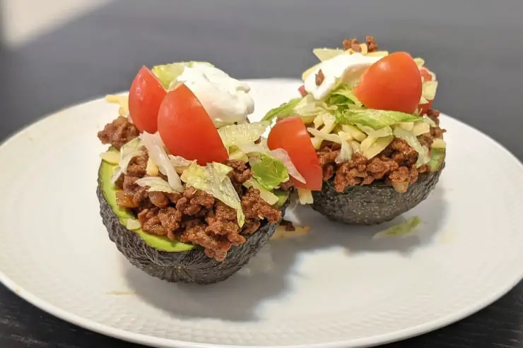 Keto taco stuffed avocados with sour cream on a white plate