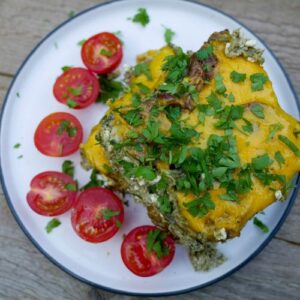 Keto sausage casserole with greens and cherry tomatoes on a white plate